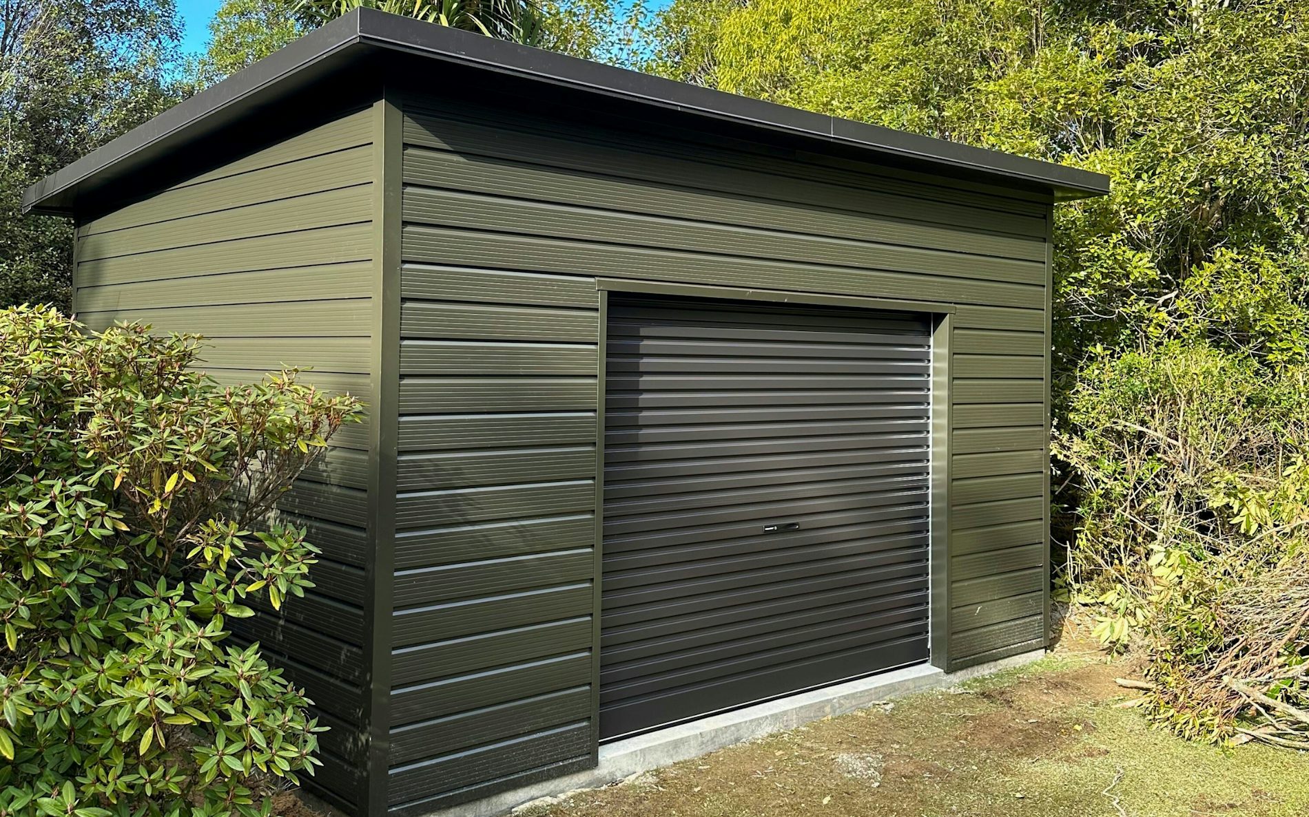 4.8m X 3.6m utility Shed, 2.4m stud Superclad cladding  in COLORSTEEL® Karaka and Roller door 2.6m wide Flaxpod